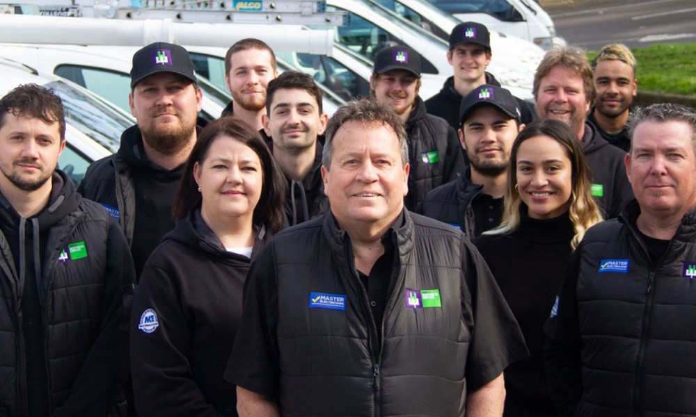 A large group of diverse service staff, including men and women, smiling and posing outdoors in front of a fleet of white service vans.